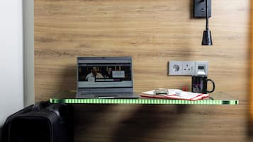 A laptop on a desk with a wooden wall, a power outlet, and a black lamp.