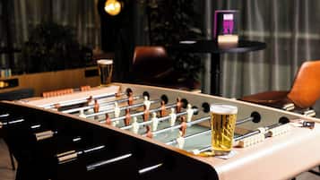 A foosball table with a glass of beer on it, a bar sign, and a chair in the background.