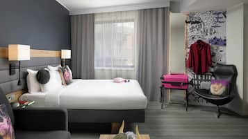 A modern hotel room with a large bed, a desk, a chair, and a small table.