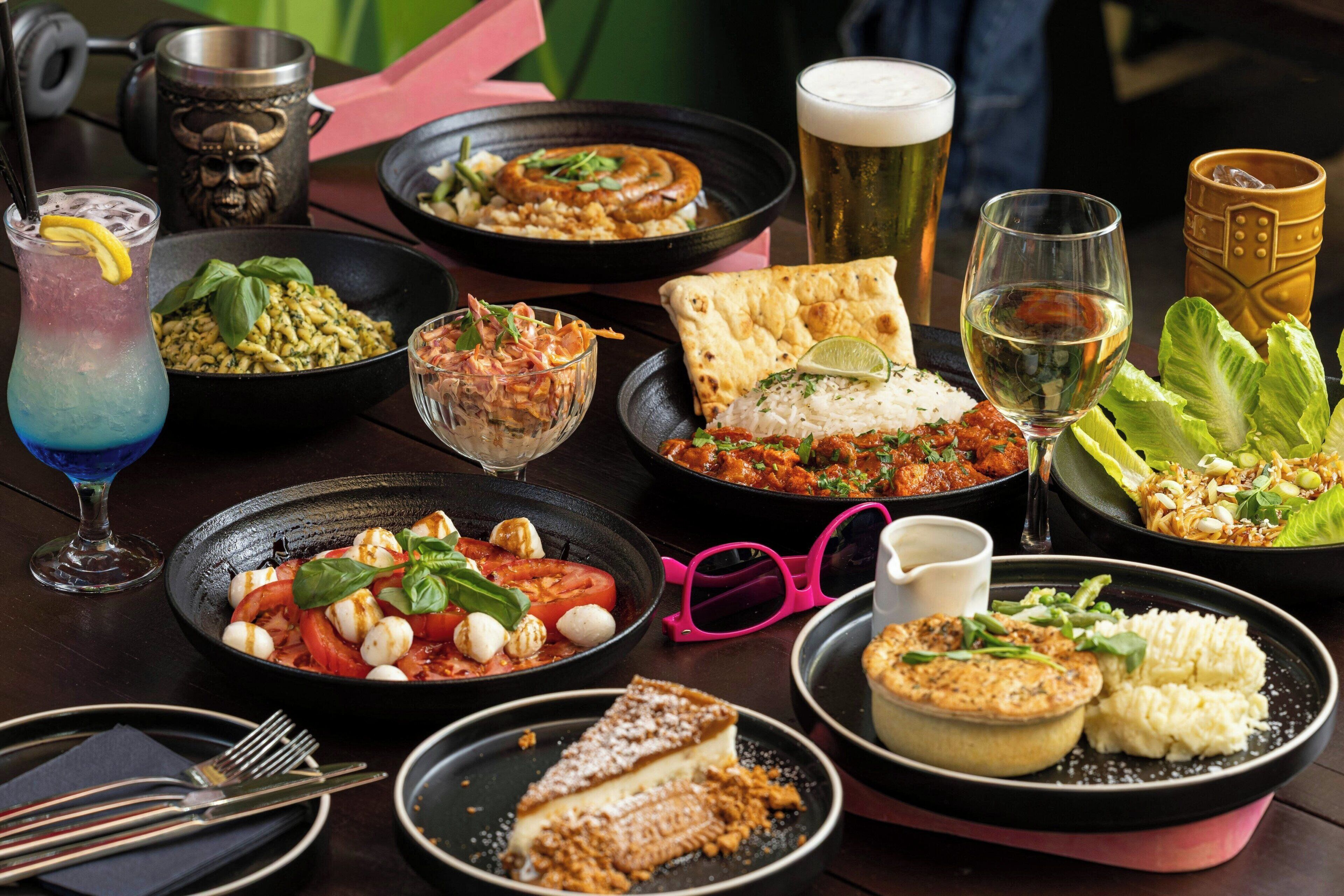 A variety of dishes and drinks on a table, including a salad, pizza, and a dessert.
