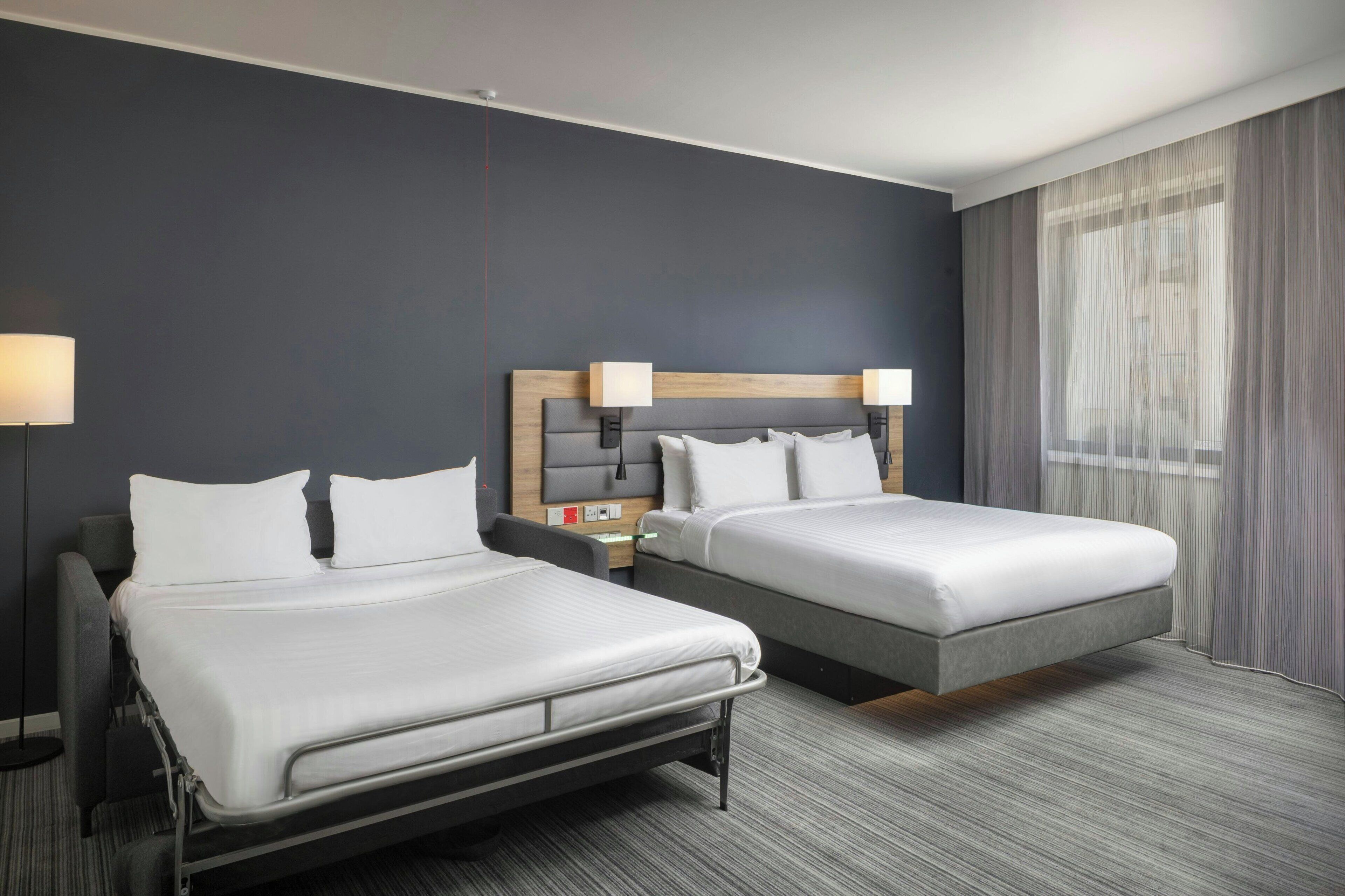A hotel room with two beds, a desk, and a lamp.