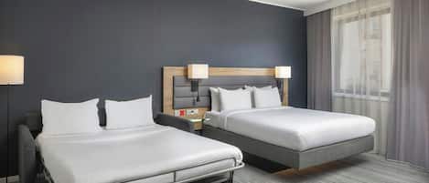 A hotel room with two beds, a desk, and a lamp.