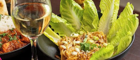 Un tazón de fideos con lechuga y semillas de sésamo, una copa de vino blanco y un plato de curry.
