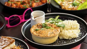 A dessert plate with a pie, mashed potatoes, and greens, accompanied by pink glasses and a small cup.