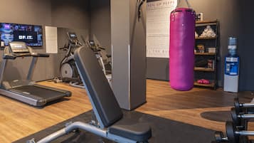 Academia com equipamentos de cardio, saco de pancada e dispensador de água.