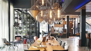 A spacious dining area with a long wooden table, modern chairs, and hanging pendant lights. - Moxy York (York)