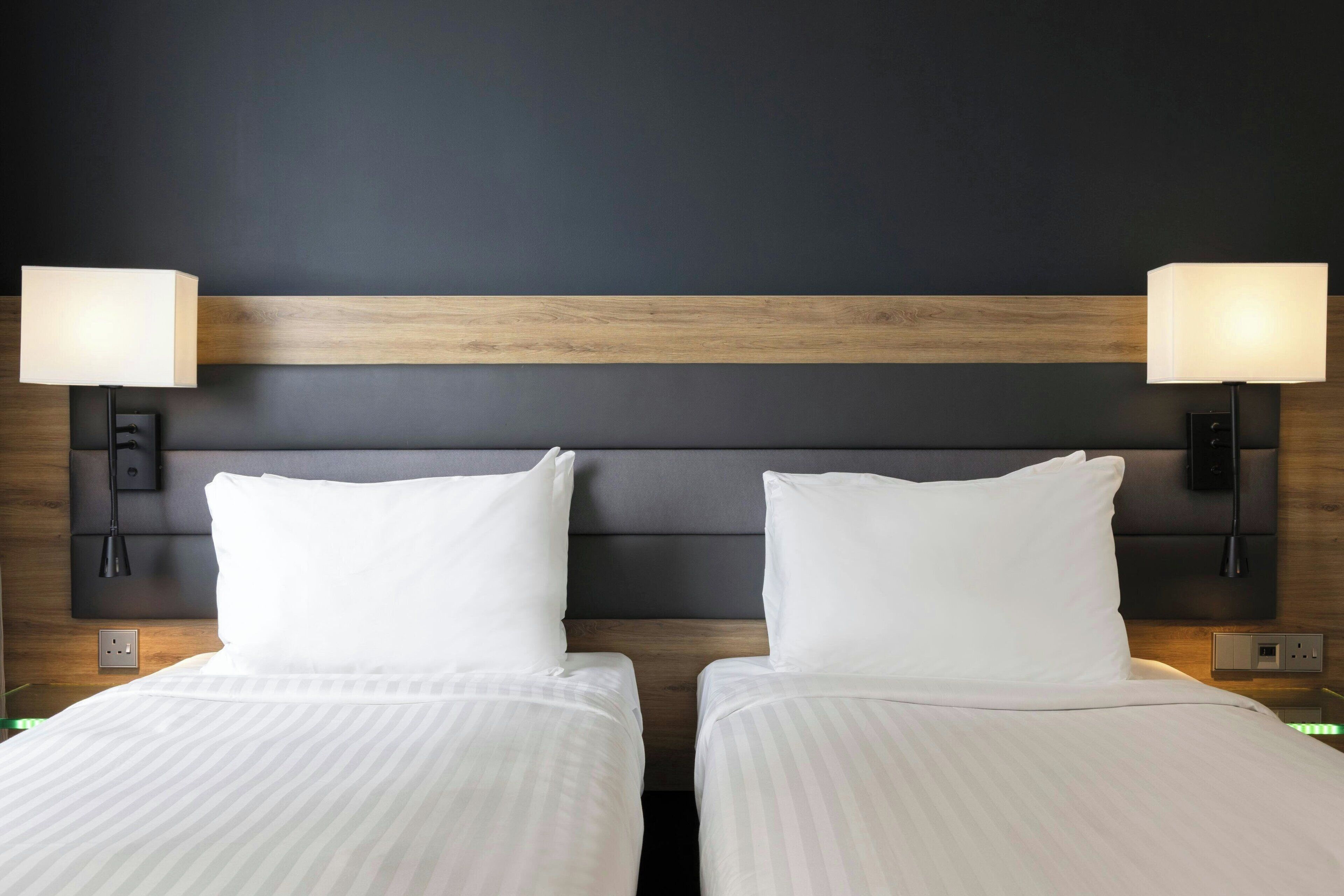 Une chambre d’hôtel avec deux lits, un mur de couleur sombre et une tête de lit en bois.
