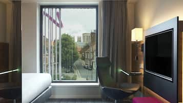 Ein Hotelzimmer mit großem Fenster, einem Bett, einem Sessel, einem Fernseher und einer Lampe.