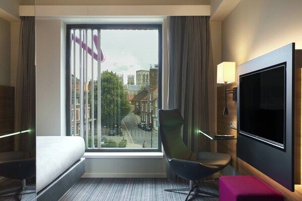 Una habitación de hotel con un ventanal grande, una cama, una silla, un televisor y una lámpara.
