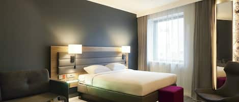 A hotel room with a bed, a sofa, a coffee table, a chair, and a large window with curtains.