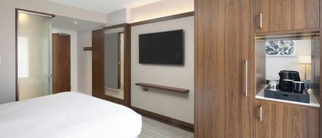 Une chambre d’hôtel comprenant un lit, un téléviseur fixé au mur, une armoire en bois et un petit coin cuisine.