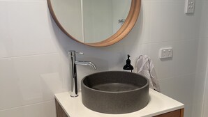 A bathroom with a round mirror, a round sink, and a wooden cabinet. - Jacaranda Place - Superior Location  (Plympton)