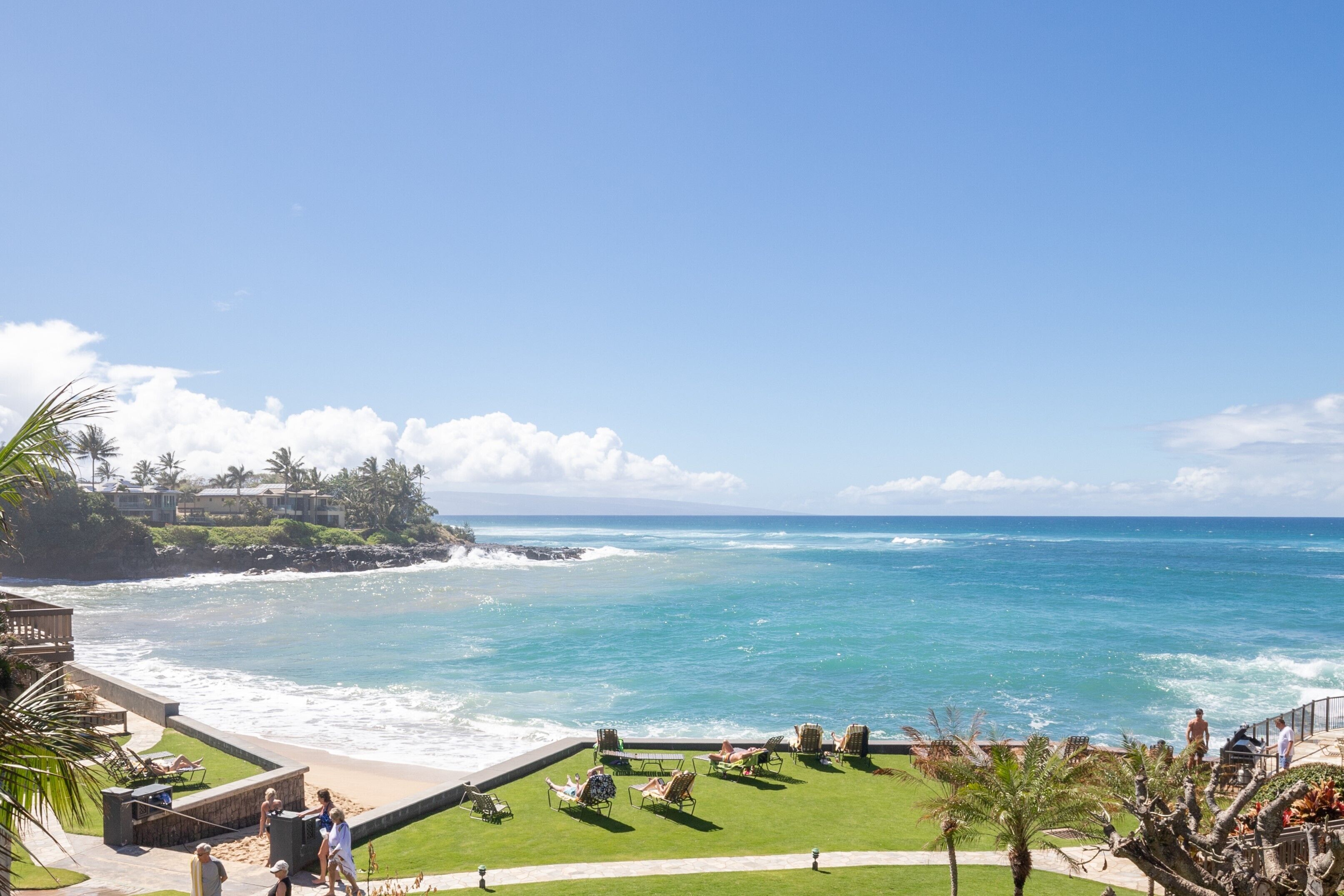 A coastal resort with a view of the ocean, a grassy area with lounge chairs, and a building with a balcony overlooking the sea.