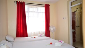A hotel room with two beds, red curtains, a fan, and a shower area. - 254 Airport Inn (Syokimau)