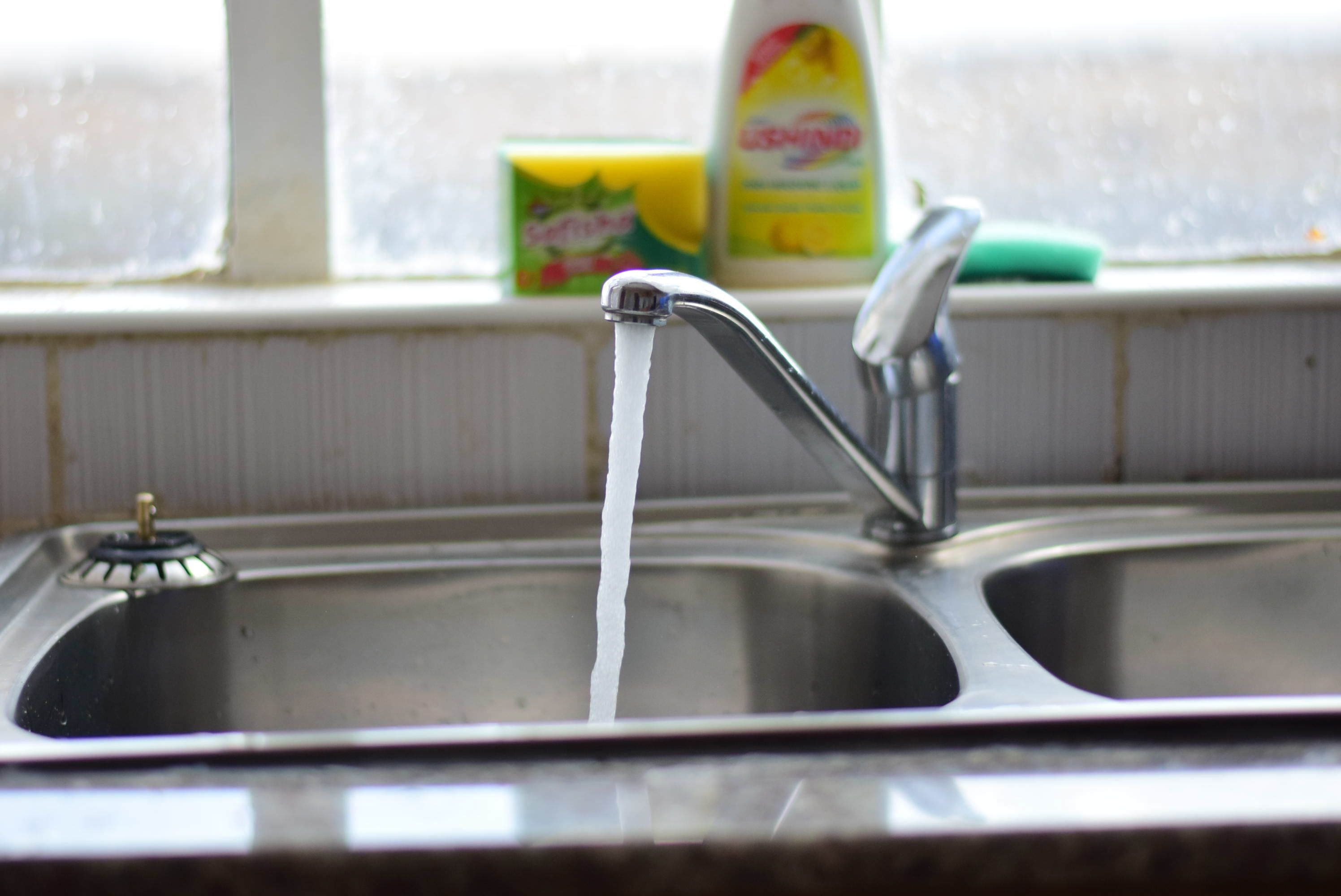 Un évier de cuisine avec de l’eau courante, un distributeur de savon et une éponge posée sur le rebord de la fenêtre.