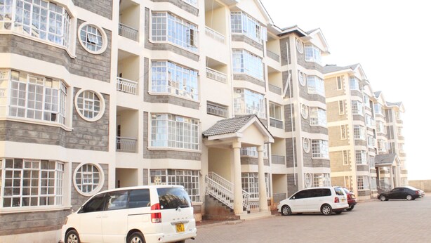 A multi-story residential building with balconies, a central staircase, and several parked cars. - 254 Airport Inn (Syokimau)