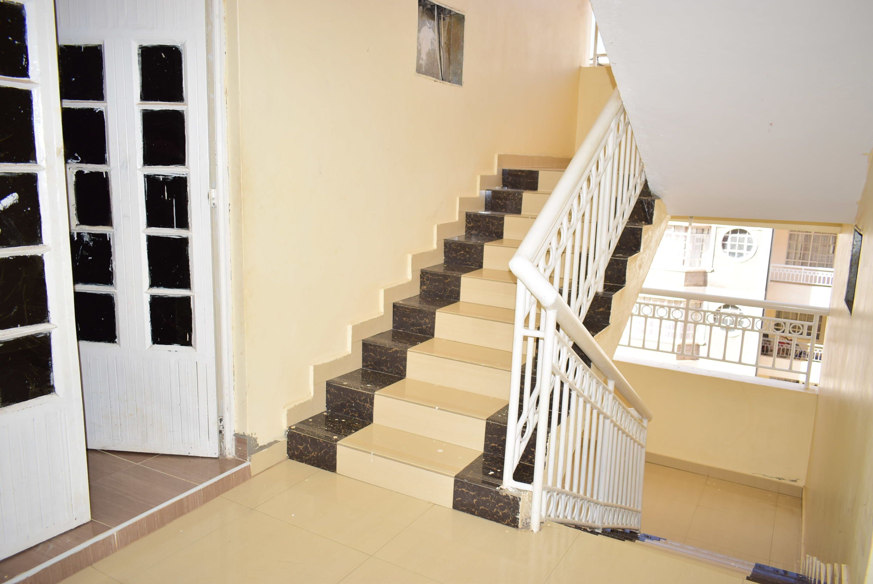 A staircase with beige and black steps, white railings, and a door with multiple windows.