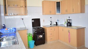 A kitchen with wooden cabinets, a stove, a sink, and a countertop with a kettle and coffee maker. - 254 Airport Inn (Syokimau)