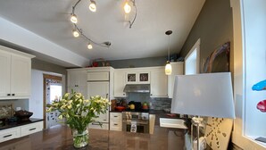 A modern kitchen with white cabinets, a marble countertop, a central island with a vase of flowers, and a pendant light above.