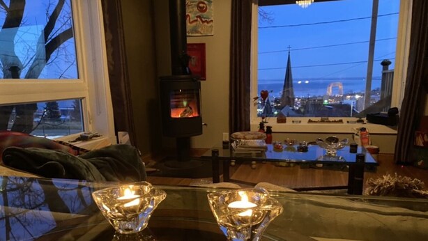 A cozy living room with a glass table, two candles, a fireplace, and a view of a bridge and cityscape through large windows.