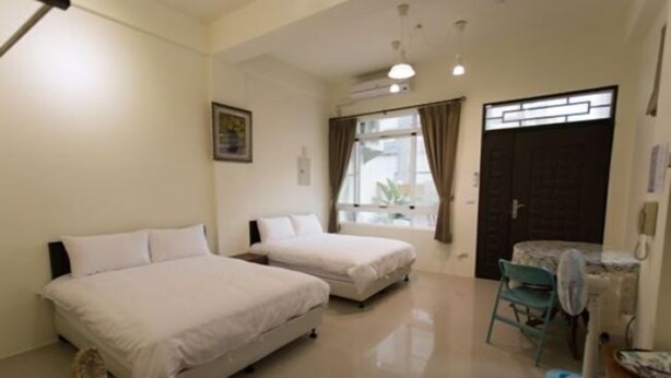 A hotel room with two beds, a small table, a chair, and a window with curtains. - Pang Mi B&B (Taitung)