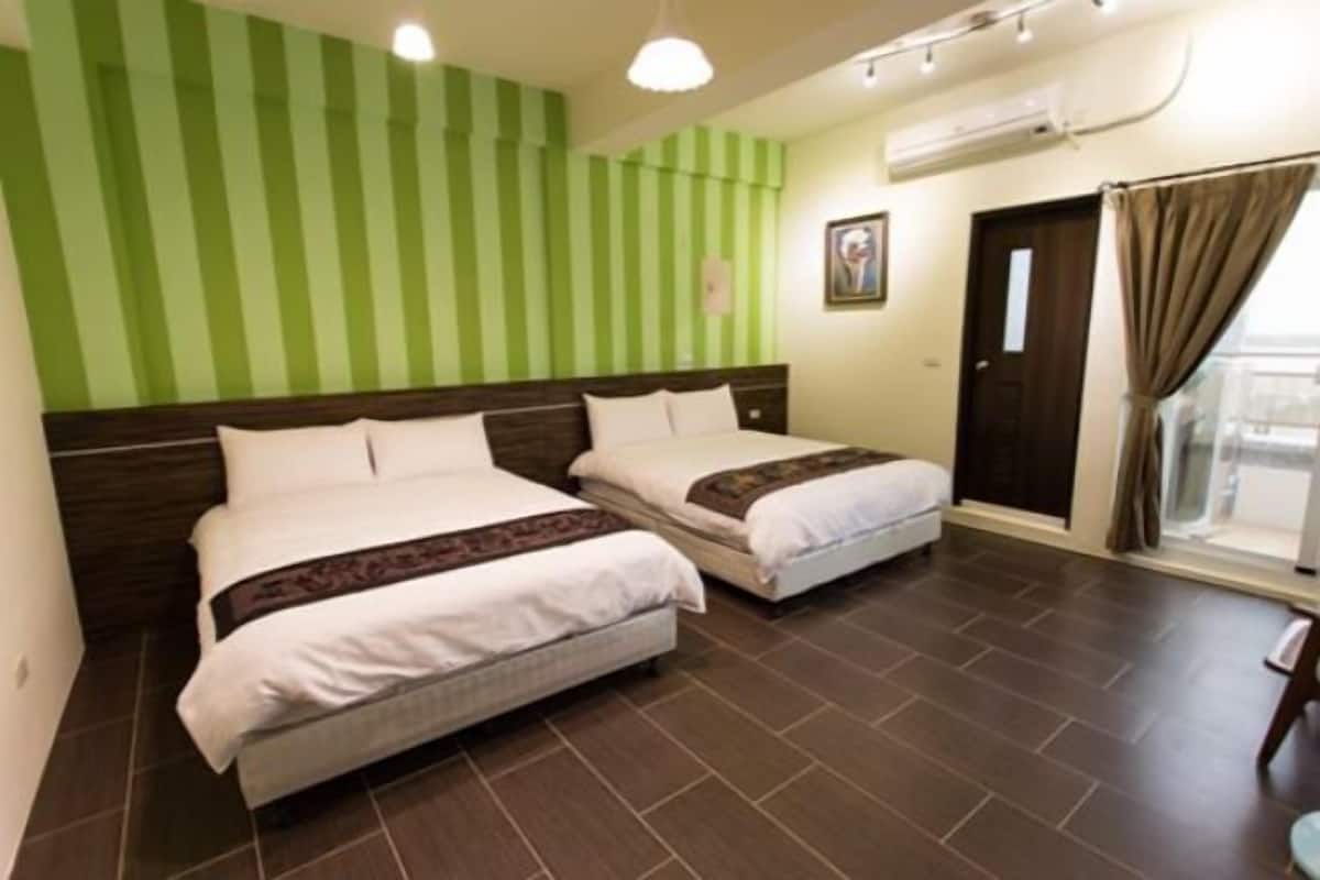 A hotel room with two beds, a green-striped wall, a window with curtains, and a door.