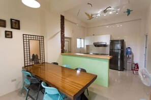 A dining area with a wooden table and blue chairs, a kitchen with a refrigerator and stove, and a ceiling with decorative bird figures. - Pang Mi B&B (Taitung)