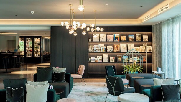 Uma área de estar moderna com bar, assentos e uma estante com livros e objetos decorativos.