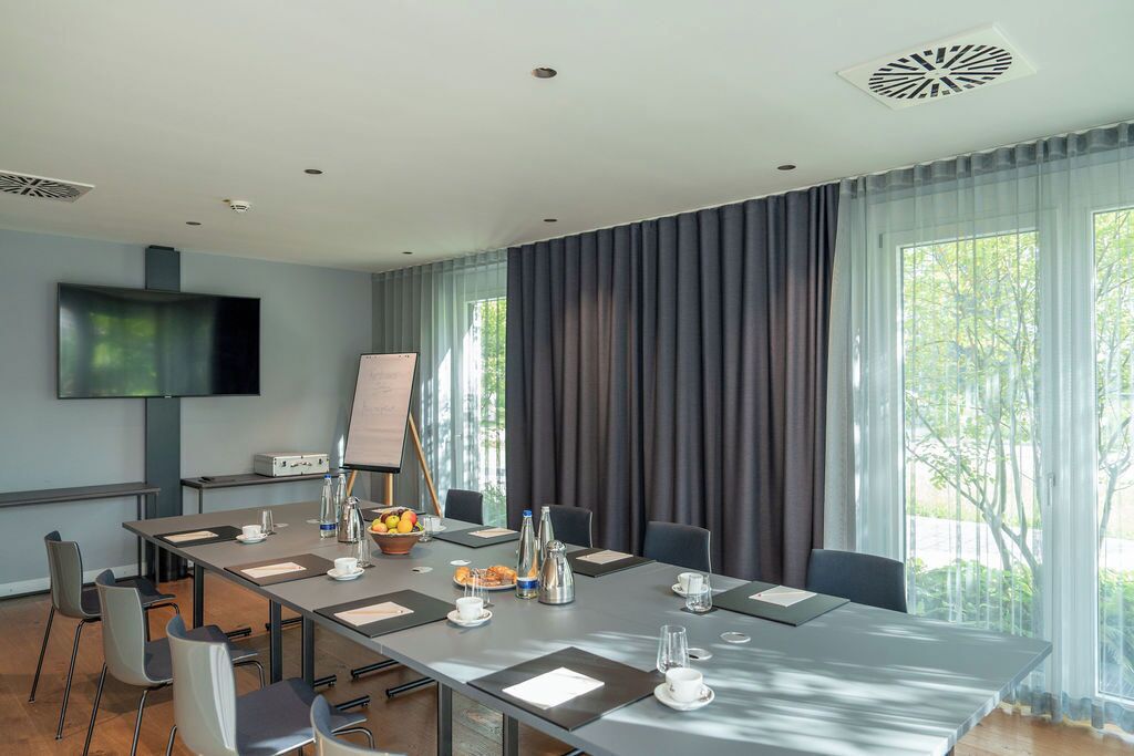 A conference room with a long table, chairs, a projector, and a large window with curtains.
