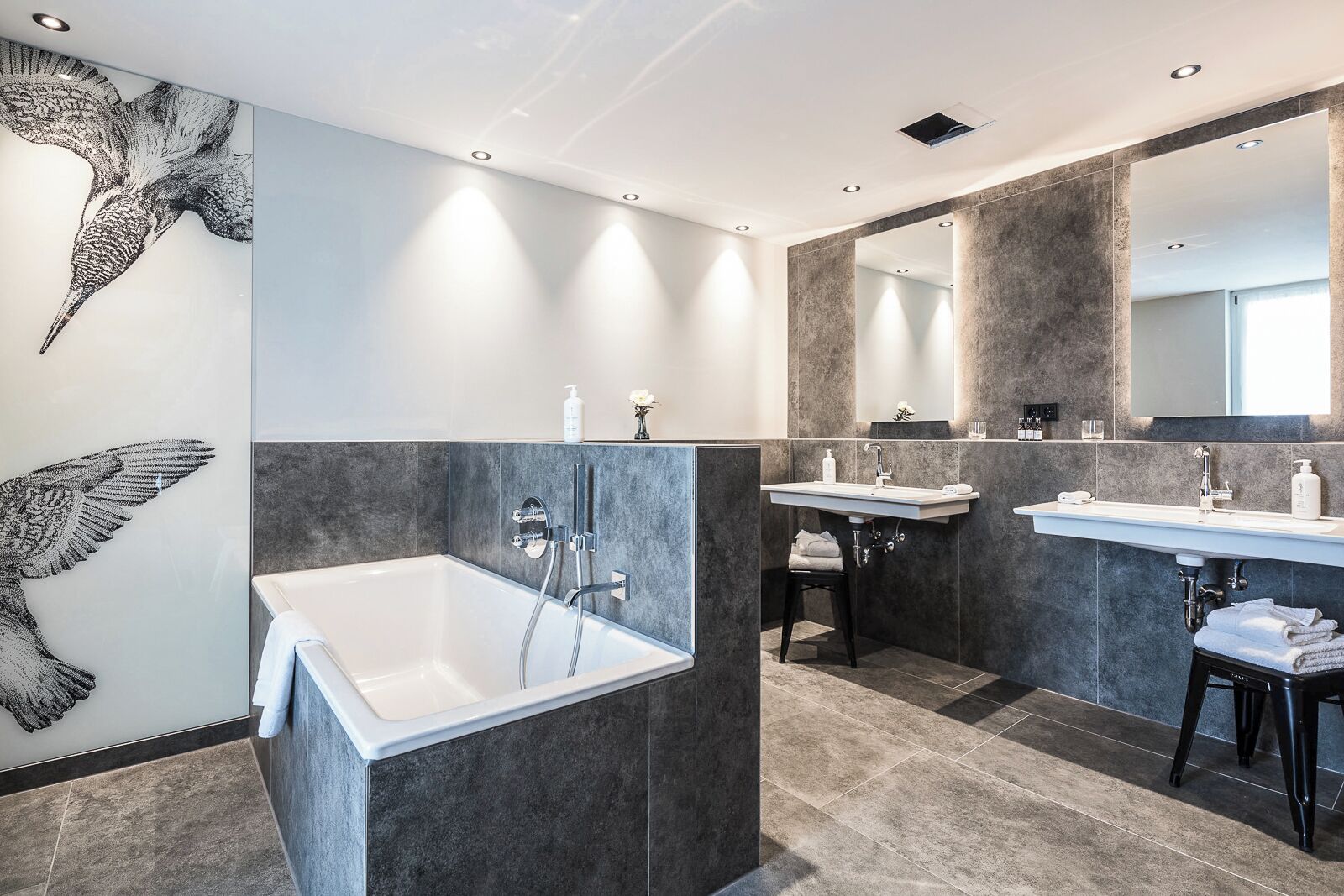 Een moderne badkamer met een groot bad, twee wastafels en een spiegel.