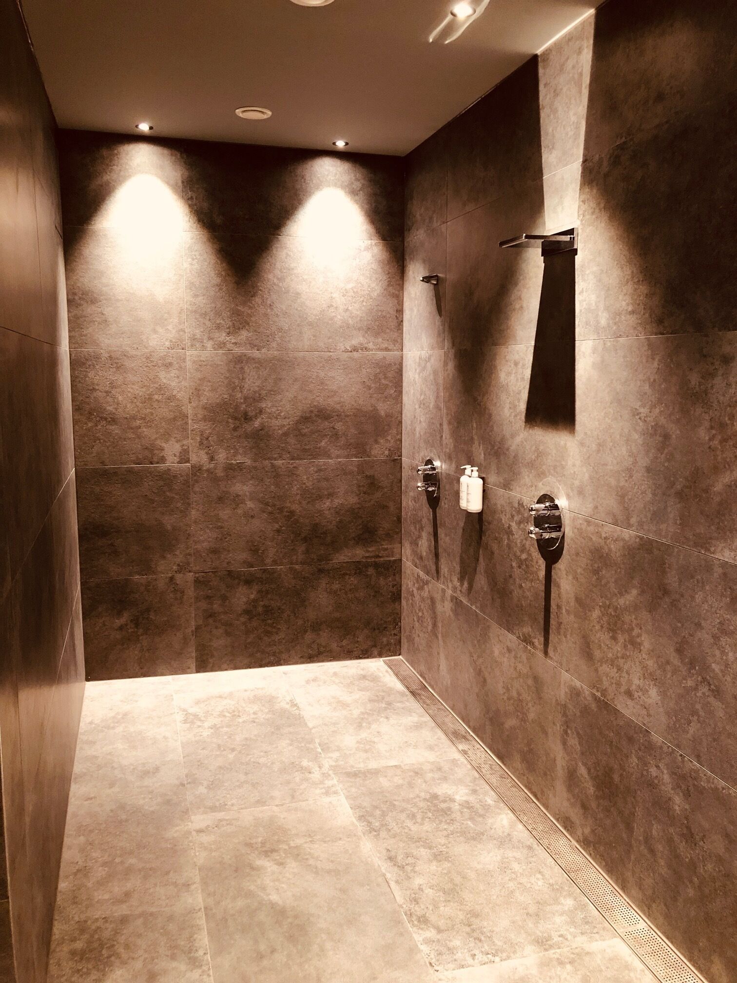 Un área de ducha moderna con azulejos oscuros, un cabezal de ducha de mano y un grifo instalado en la pared.