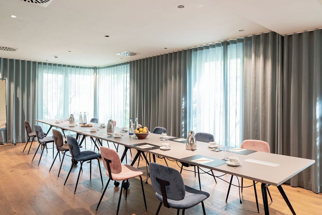 Un salón de conferencias con una larga mesa, sillas y un amplio ventanal con cortinas.