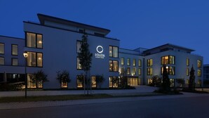 Um hotel moderno com um logotipo em destaque, várias janelas e uma entrada bem iluminada.