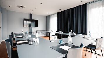 A modern conference room with a long table, chairs, and a flat-screen TV on the wall.