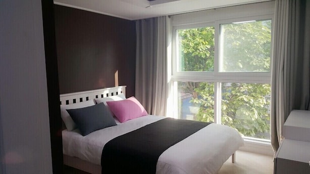 Ein Schlafzimmer mit Bett, einem Fenster mit Vorhängen und Blick auf Grün.