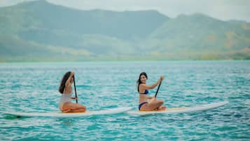 Dos personas en tablas de paddleboard sobre un cuerpo de agua con montañas al fondo.