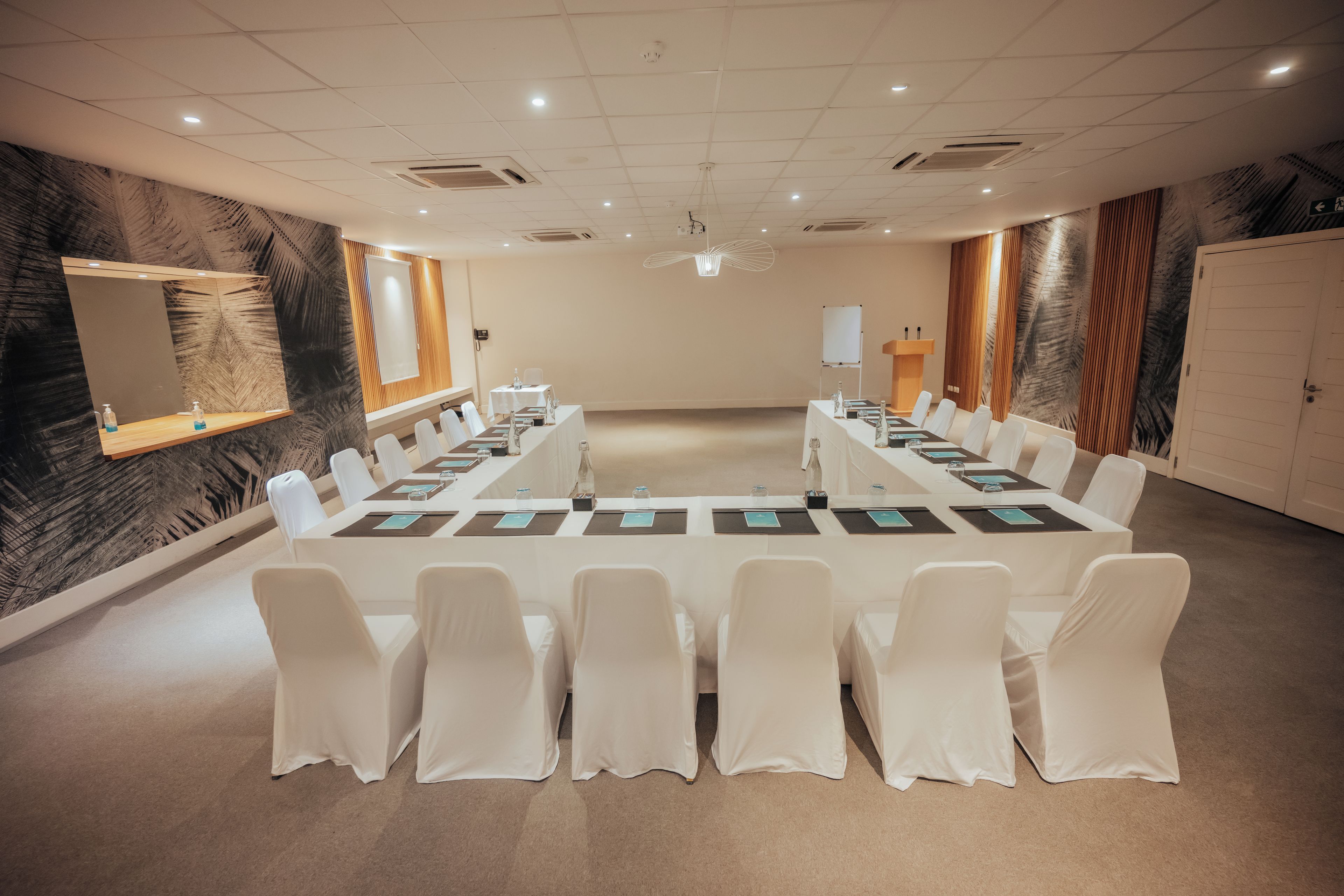 Un salón de conferencias con una larga mesa, sillas blancas, una pizarra y un atril.