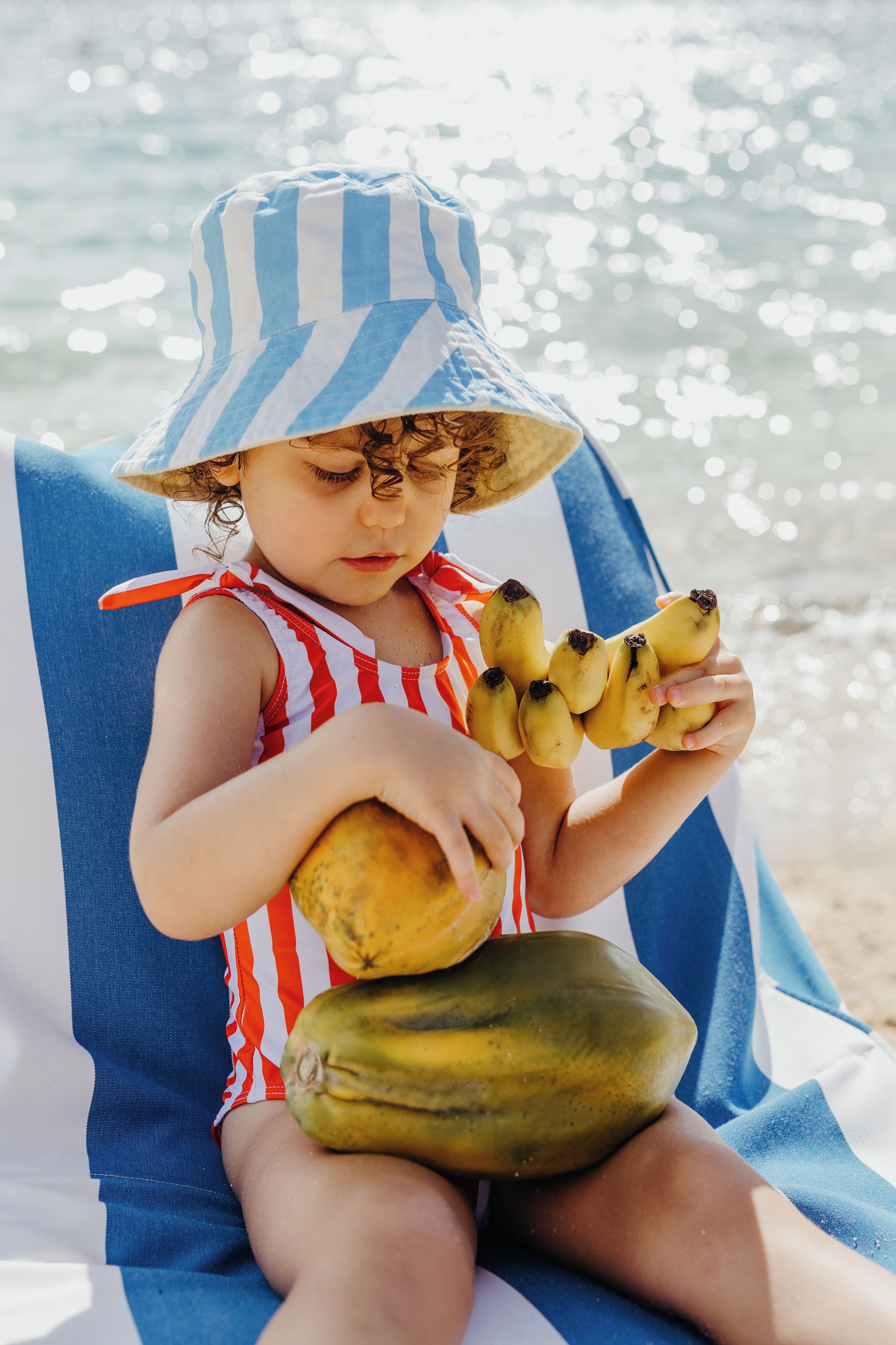 Un enfant assis sur une chaise de plage, tenant des bananes.