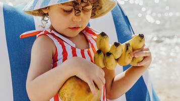 Un enfant assis sur une chaise de plage, tenant des bananes.