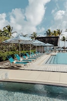 Una piscina al aire libre, sombrillas, sillones reclinables de piscina