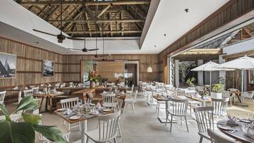 Un restaurant spacieux aux murs en bois et au plafond haut, comprenant plusieurs espaces de restauration avec des chaises et des tables blanches.