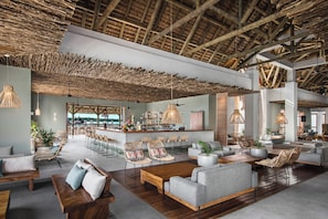 A spacious lounge area with a high ceiling, wooden beams, and a bar with bar stools. - Preskil Island Resort (Mahebourg)