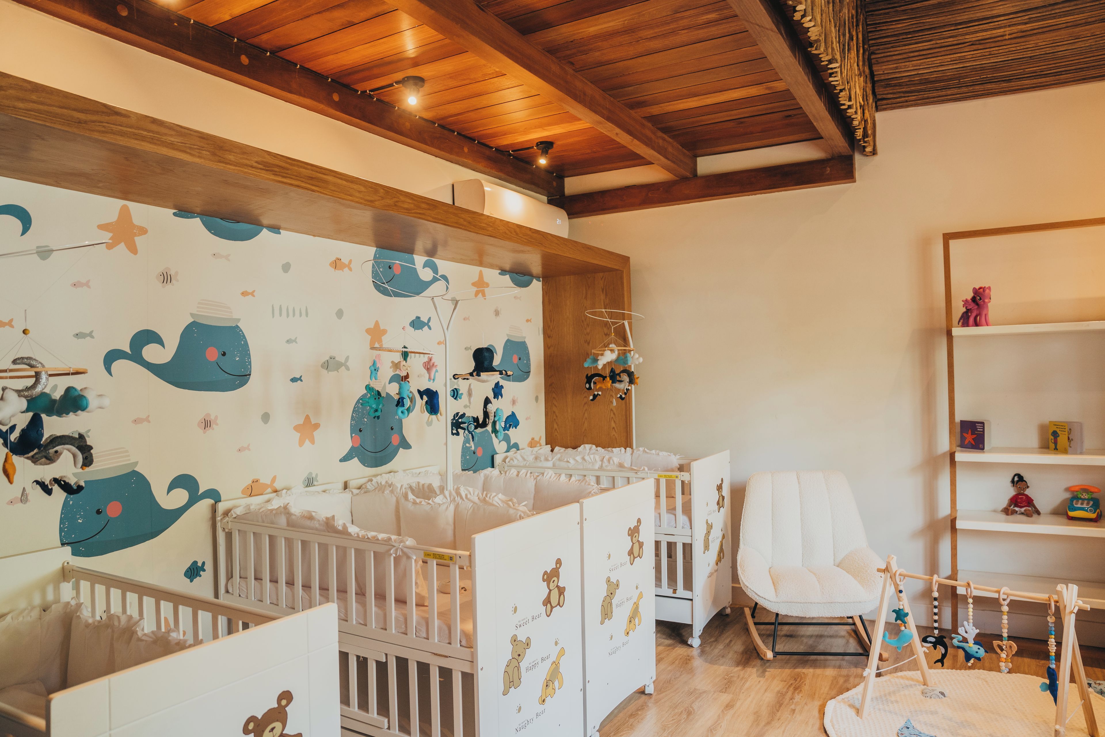 A baby room with cribs, a rocking chair, and a wall with a nautical theme.