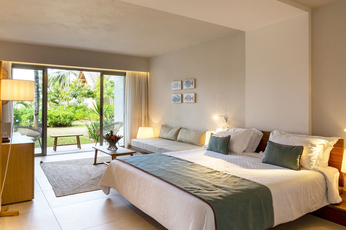 A hotel room with two beds, a desk, and a view of a garden.