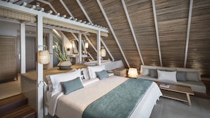 An attic bedroom with a high ceiling, a bed with a green blanket, a sofa, a small table, and a ceiling fan.