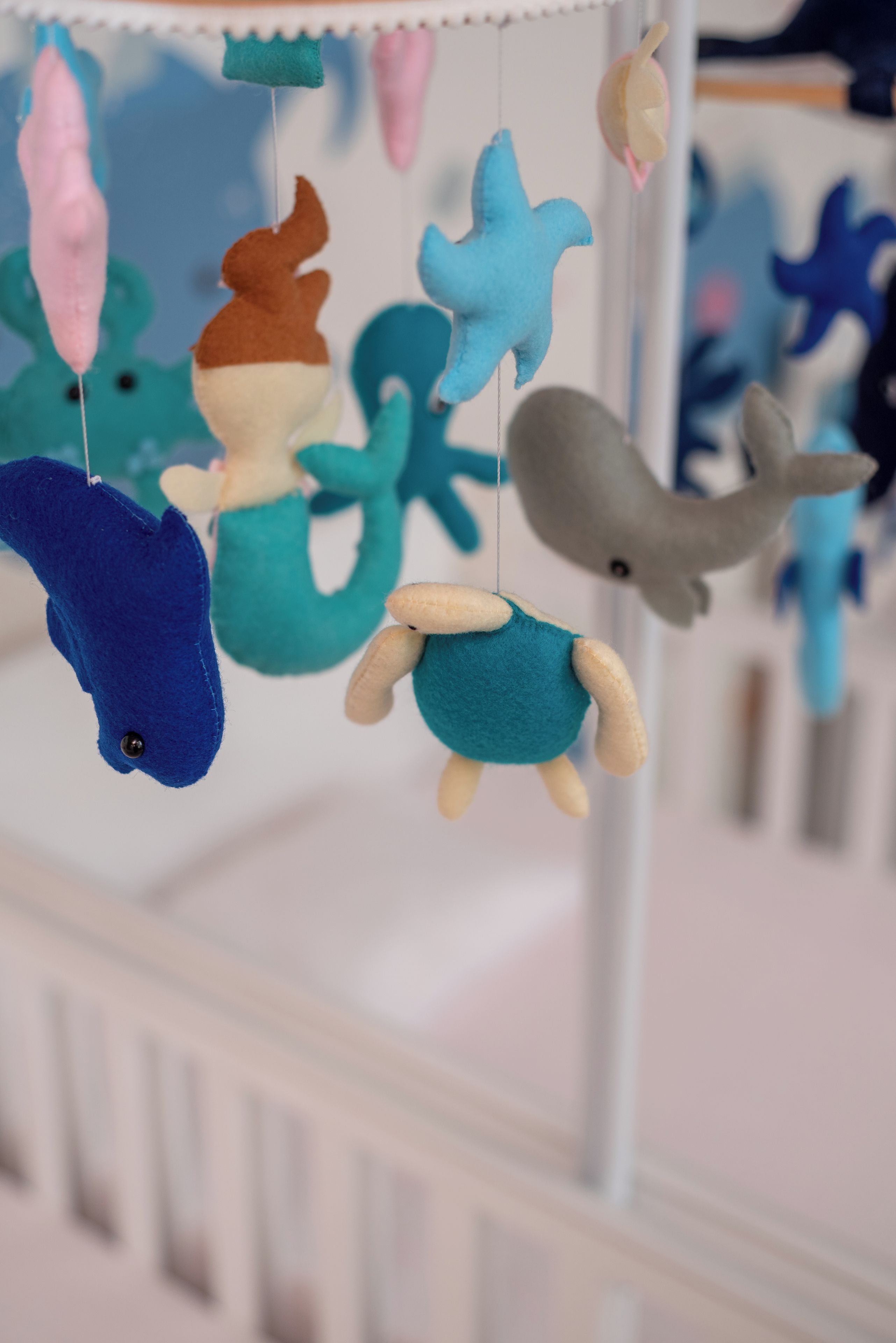 A crib with a white railing and a hanging mobile featuring various animal figures.