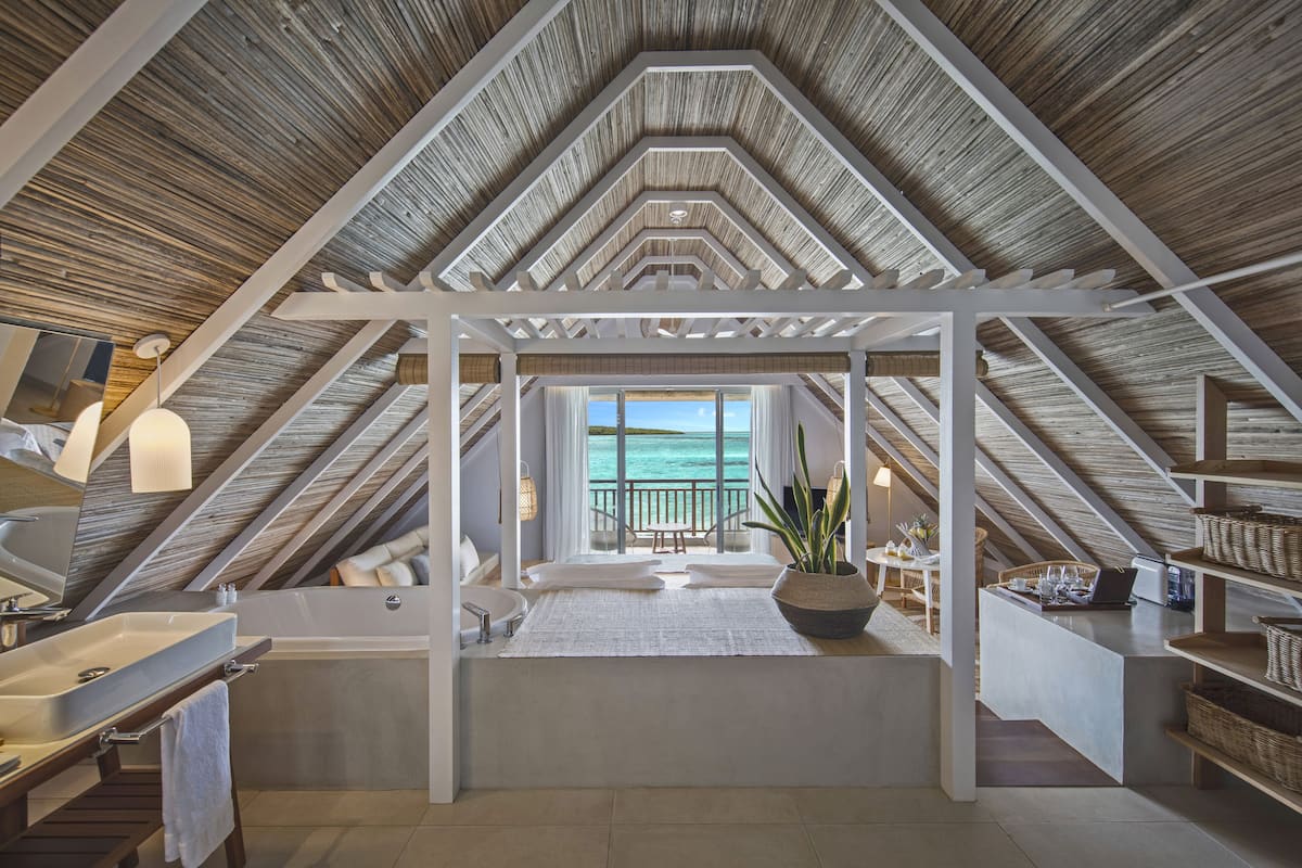A high-ceilinged attic bedroom with a view of the sea, a built-in bathtub, and a workspace area.
