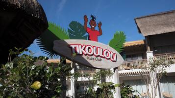 A sign for 'TIKOULOU Kids Club' with a tropical theme, including a stylized palm tree and a child waving.