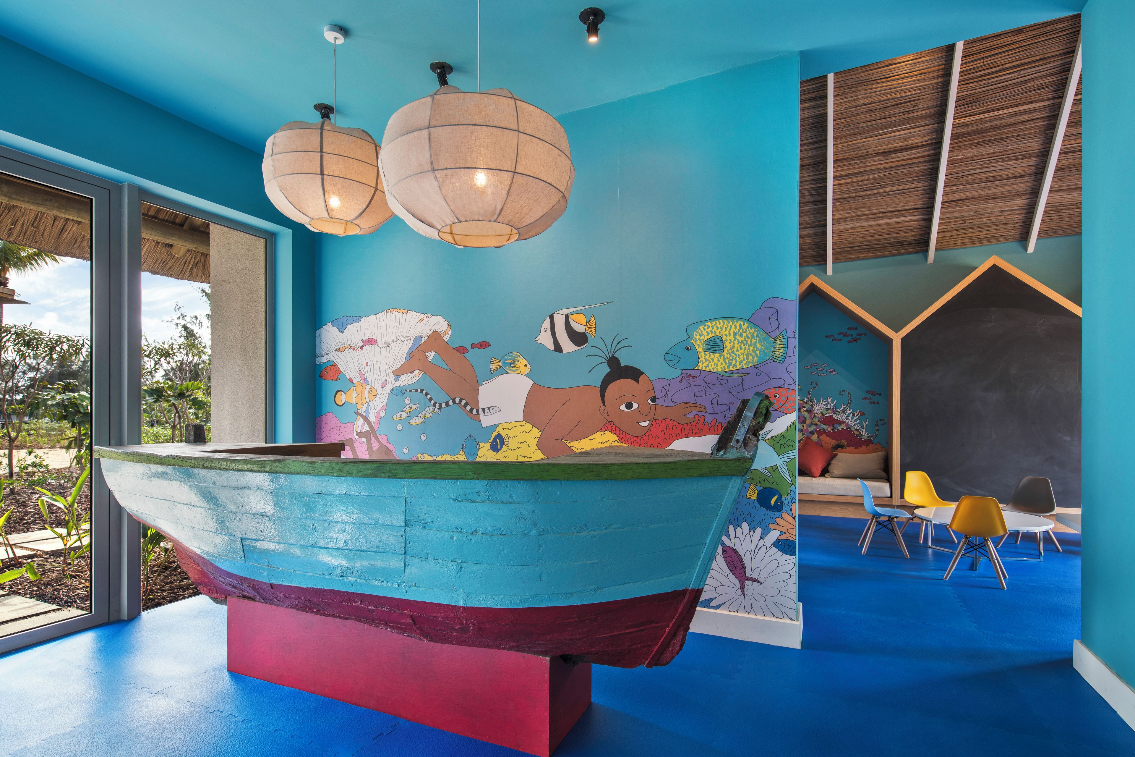 Una habitación con un gran mural de peces de colores vivos en la pared, una bañera en forma de barco original y una zona de estar con sillas y un sofá.
