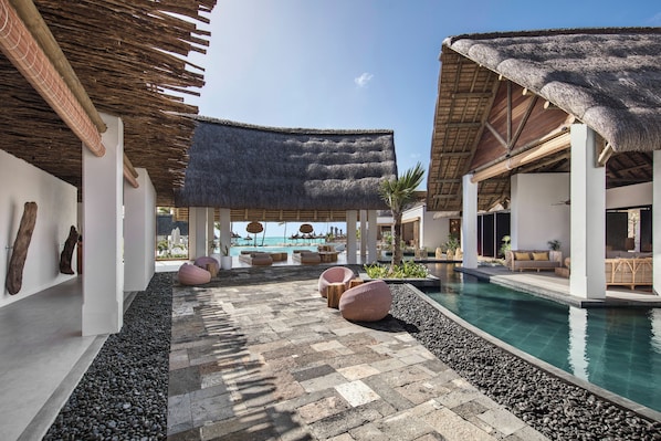 A resort pool area with thatched-roof structures, seating, and a clear view of the ocean. - Preskil Island Resort (Mahebourg)